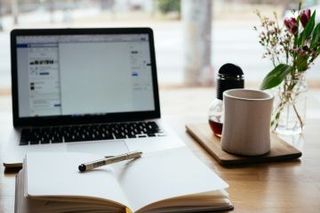 A desk with a notebook open in front of a laptop