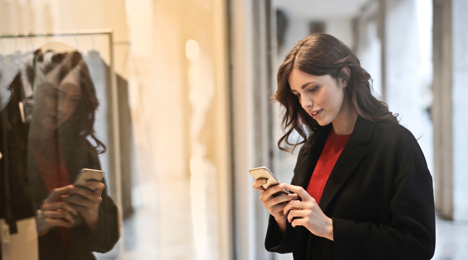 Woman holding a phone in her hand standing in front of a store window