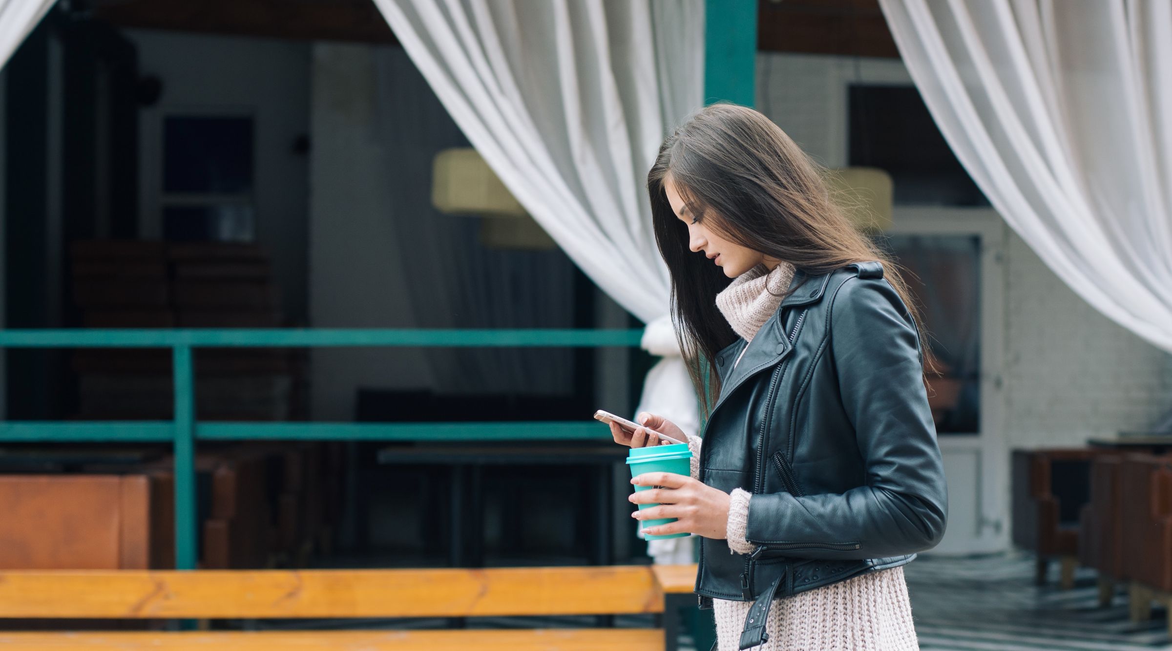 Woman holding coffee in her left hand looking at her phone in her right hand