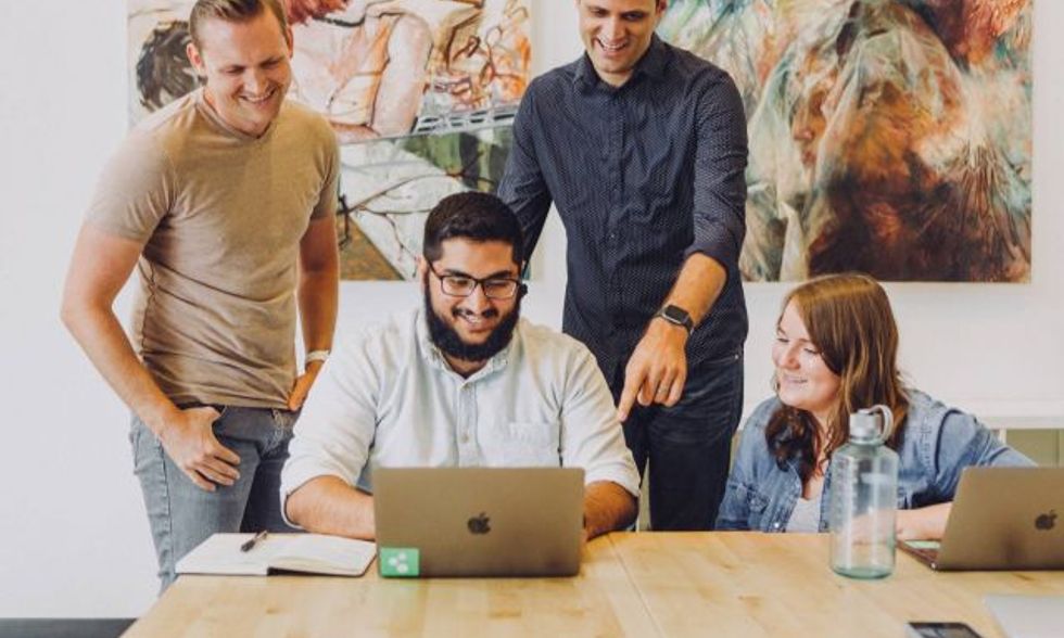 Four people sitting at a table looking at a laptop