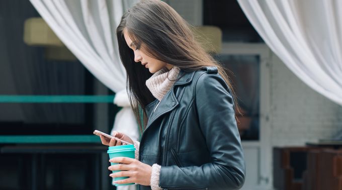 Woman holding coffee in her left hand looking at her phone in her right hand