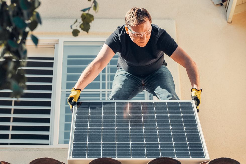 Man holding a solar panel on a roof