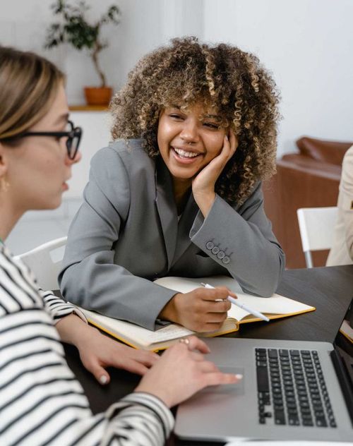 woman smiling and looking at her collegue explain somthing of the laptop